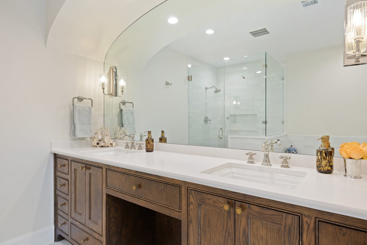 Bathroom with double vanity, dark wood cabinetry, large mirror, and glass-enclosed shower.