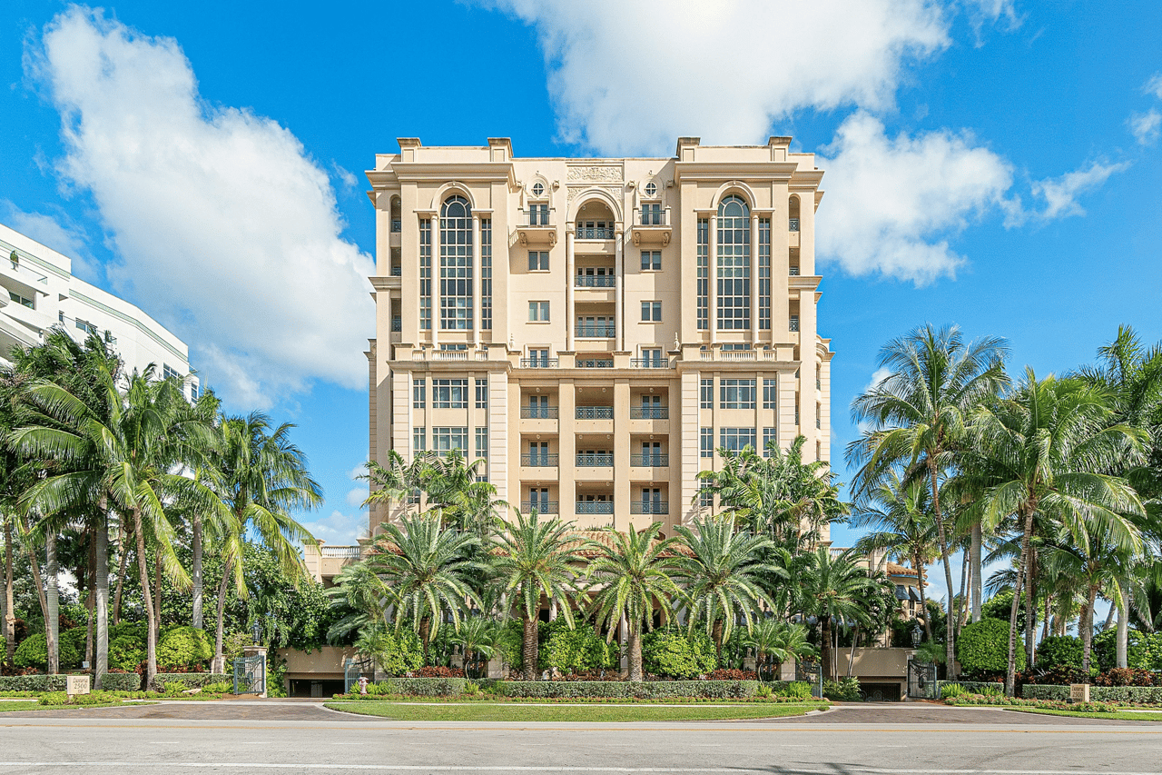 Luxuria condominium framed by palm trees, with arched windows and balconies.