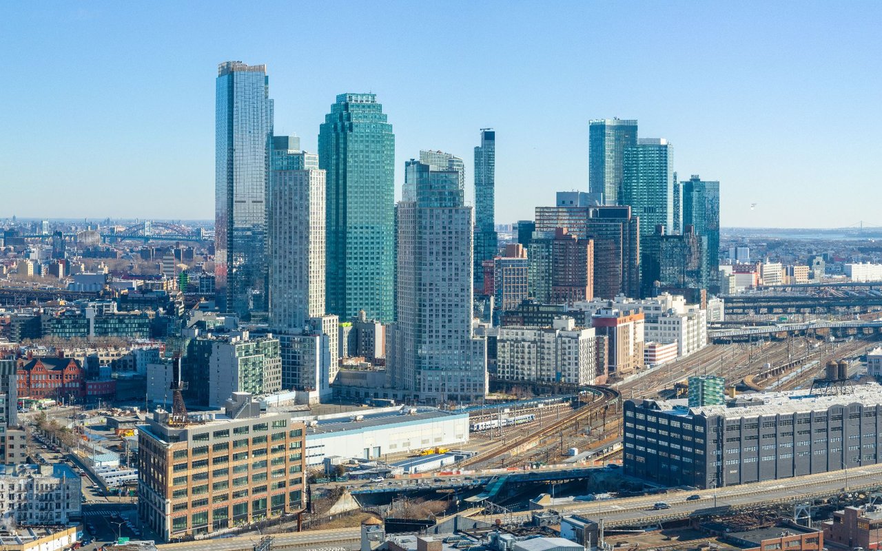 Long Island City skyline with glass high-rises and railway tracks in the foreground.