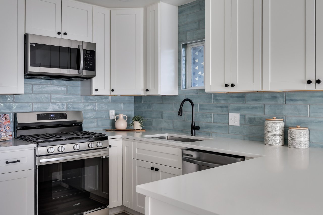 Kitchen with white cabinets, blue-gray tile backsplash, stainless steel appliances, and a white peninsula.
