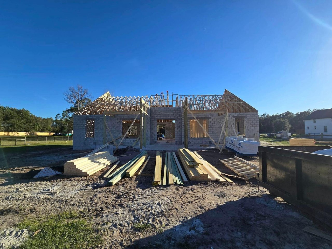 House under construction with block walls, exposed roof framing, and lumber stacked in front.