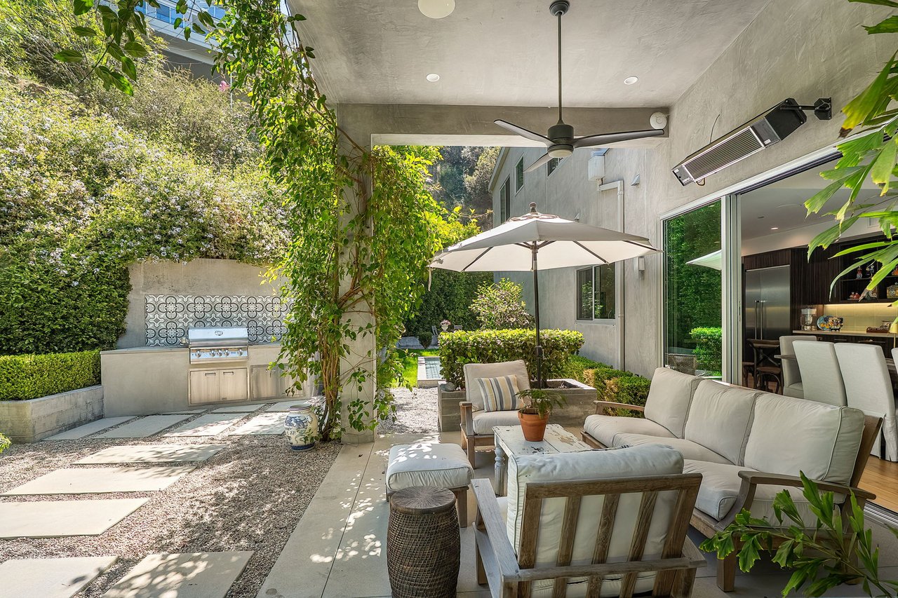 Outdoor patio with cushioned seating, a large umbrella, built-in grill, and leafy courtyard garden.