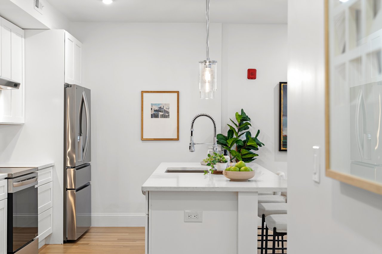 Bright white kitchen with a large island, stainless-steel appliances, and a spring-coil faucet.