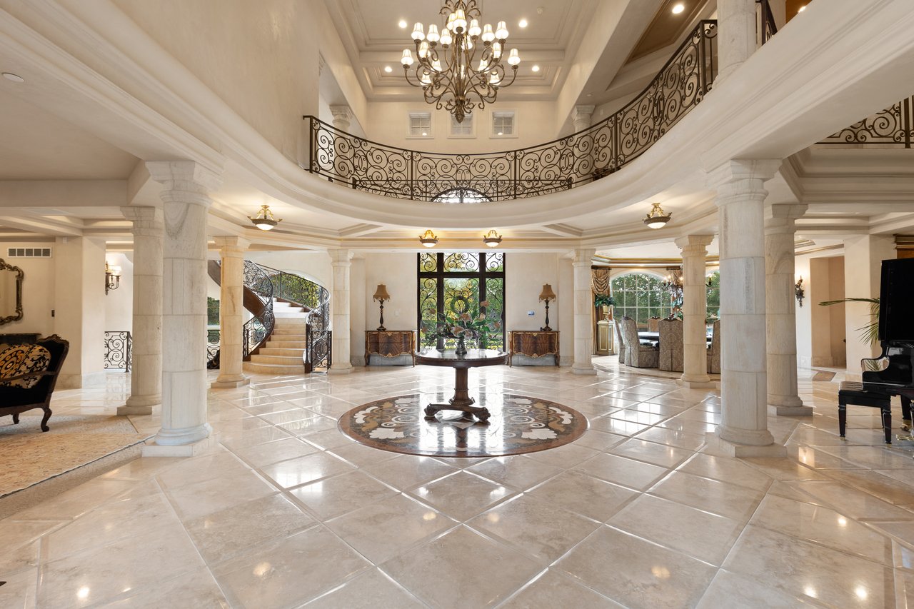 Grand foyer with a marble floor, ornate chandelier, curved wrought-iron balconies, and sweeping staircase.