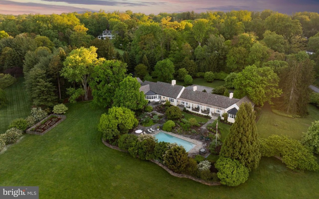 Aerial view of a long home amid autumn trees, with a swimming pool and landscaped grounds.