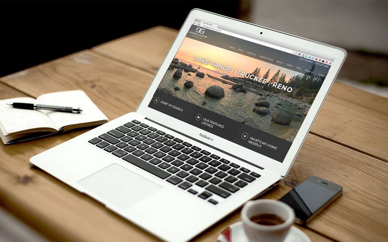 Laptop displaying a Lake Tahoe real estate website beside coffee, phone, and notebook.