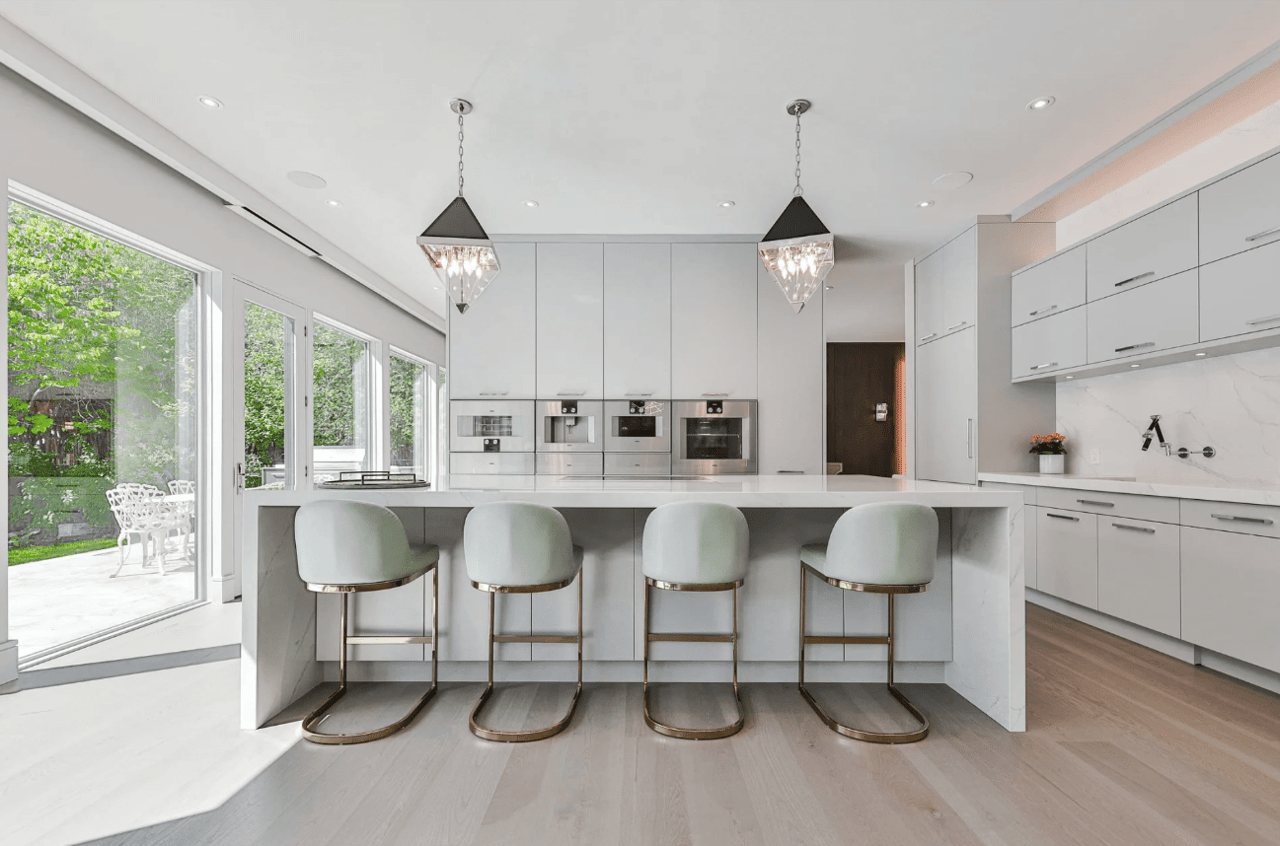 A sleek kitchen with a big island with white quartz countertops and 4 stools