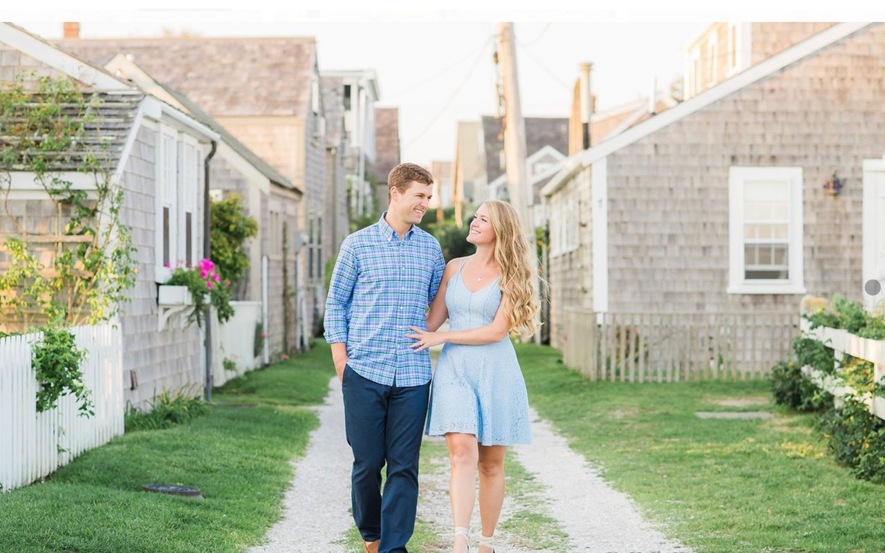 Man and woman smiling and walking down a path in between rows of houses in Nantucket.