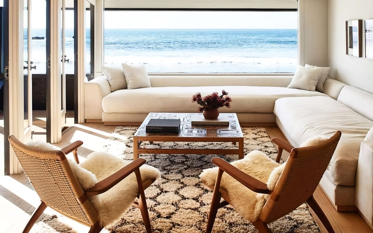  A sunlit, coastal living room with a relaxed and luxurious atmosphere. Large glass doors frame a stunning ocean view.