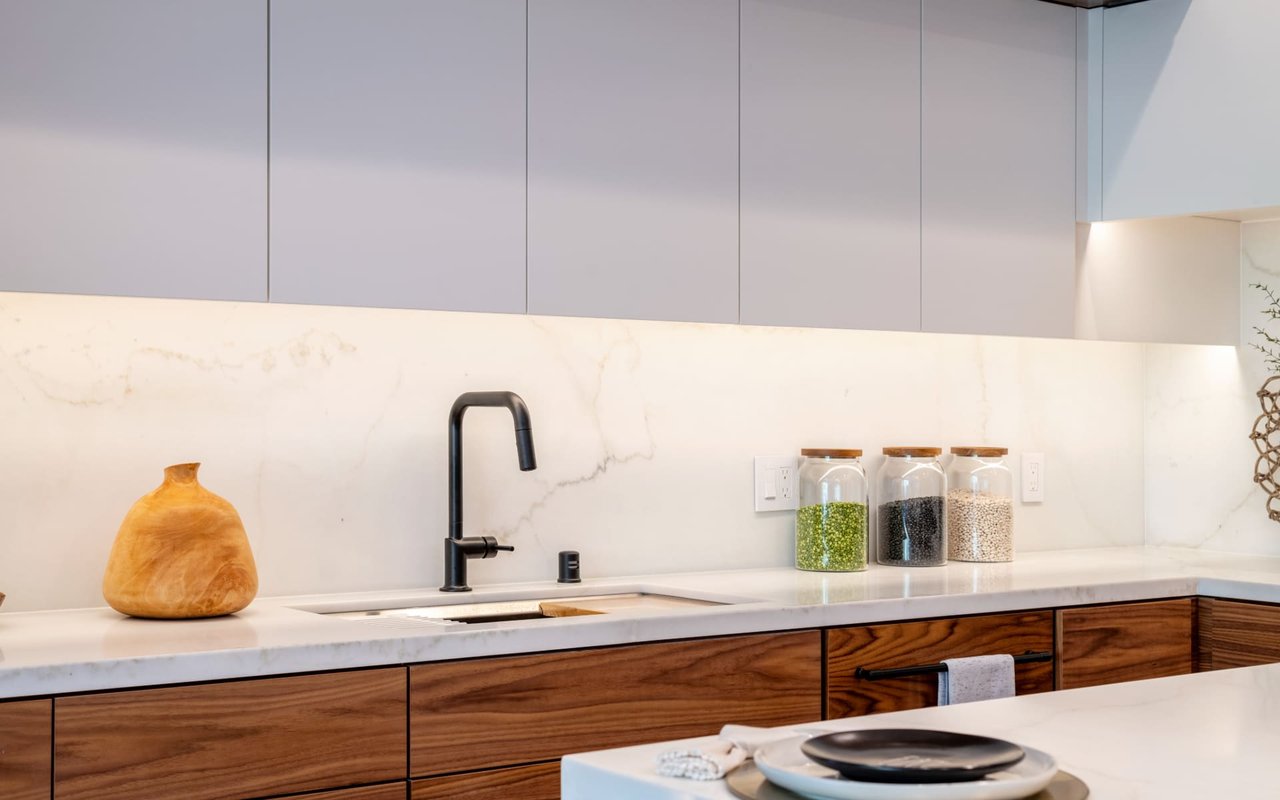 Modern kitchen with walnut cabinets, a pale stone backsplash, and a matte black faucet.
