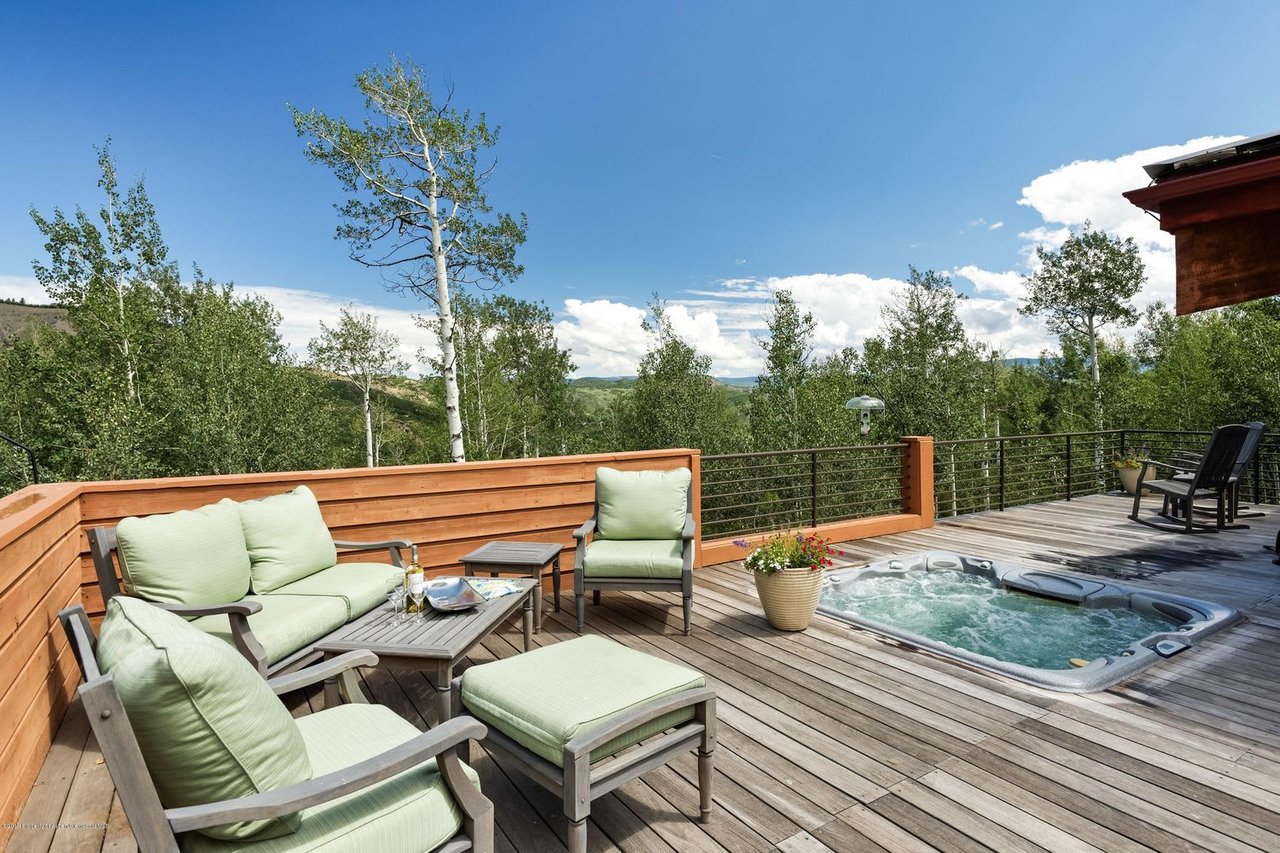 Wooden deck with a hot tub and pale green seating overlooking wooded hills.