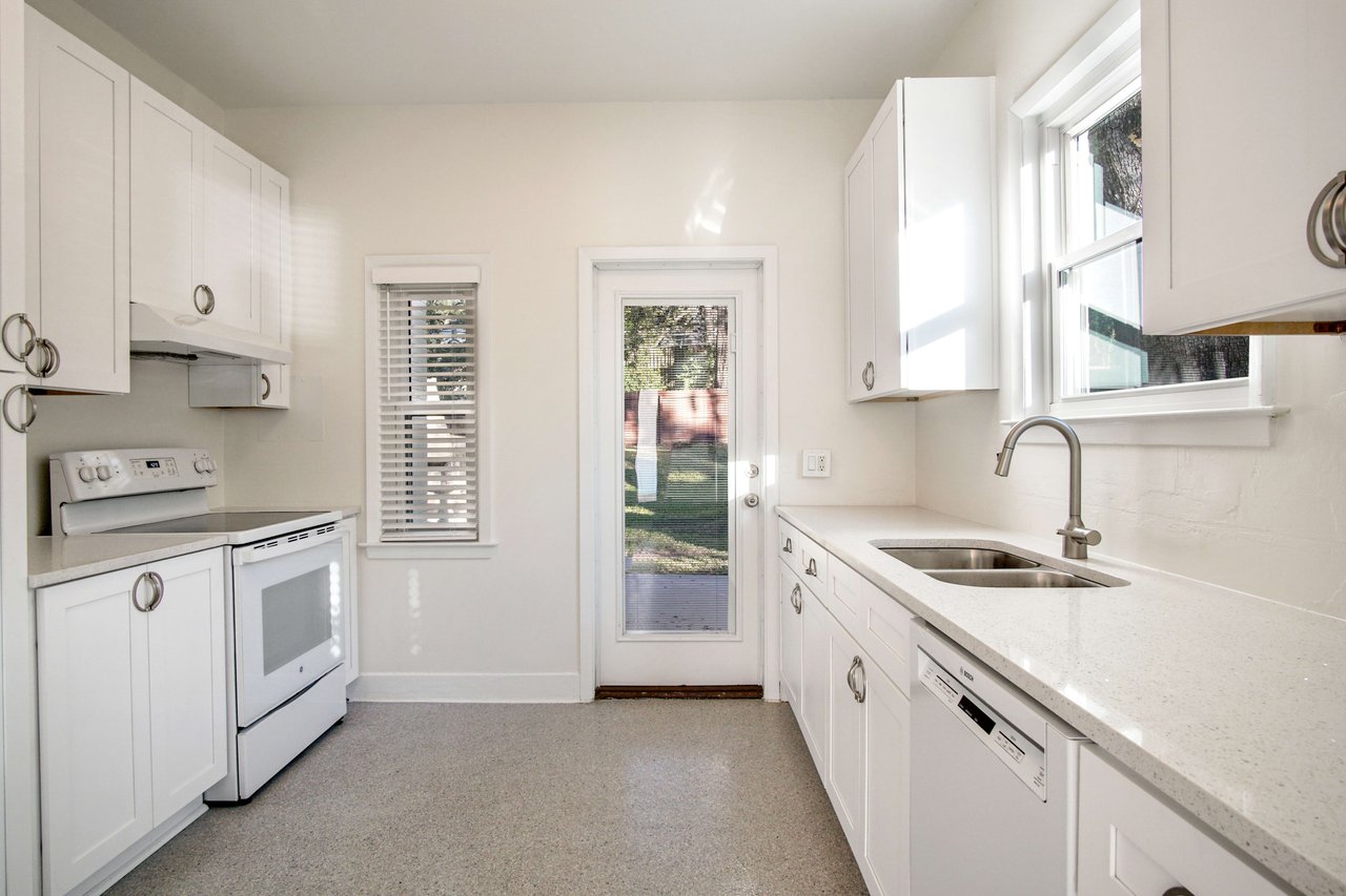 A comprehensive view of the kitchen, showing the refrigerator, stove, sink, and cabinets. The kitchen has a door leading outside and is designed with white fixtures and ample counter space.