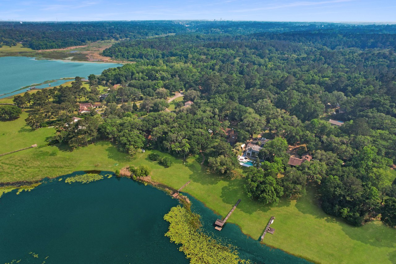 An aerial view of the Lake Breeze community, featuring houses near a large body of water and surrounded by lush greenery.