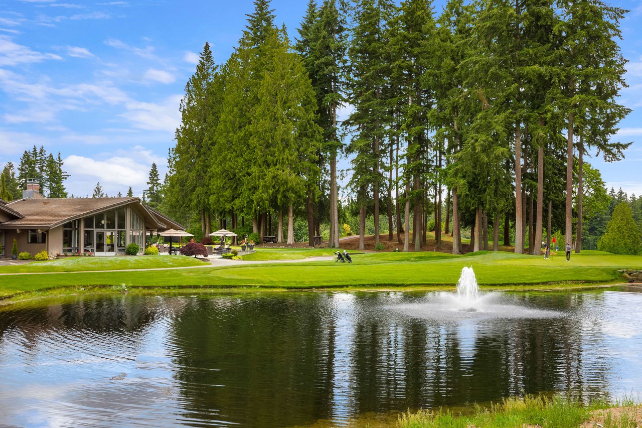 A scenic golf course with a pond in the foreground and a clubhouse in the background