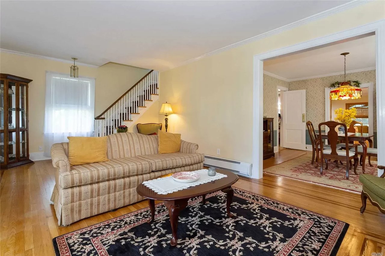 Living room with a striped sofa, floral rug, staircase, and view into the dining room.