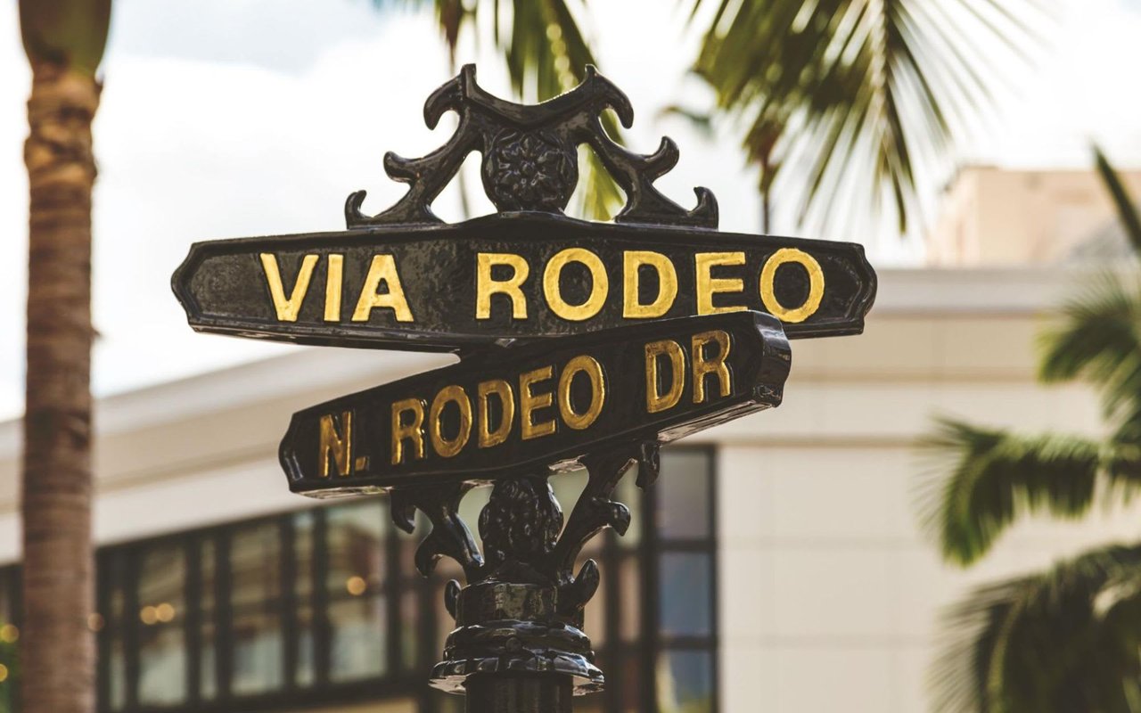  A close-up view of a black cast-iron street sign with ornate detailing, featuring two directional arrows with raised gold lettering. 