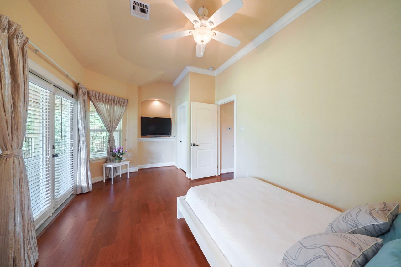 Large bedroom with double doors that lead to back balcony. It has a TV niche, window nook, & cedar lined ceiling walk-in closet.