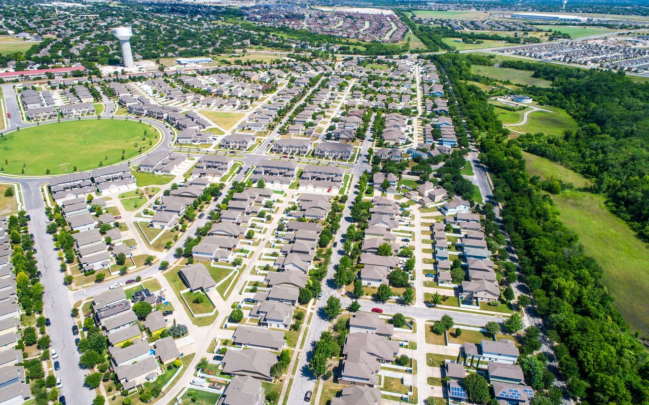 Aerial view of a suburban neighborhood beside a grassy park and tree-lined greenbelt.