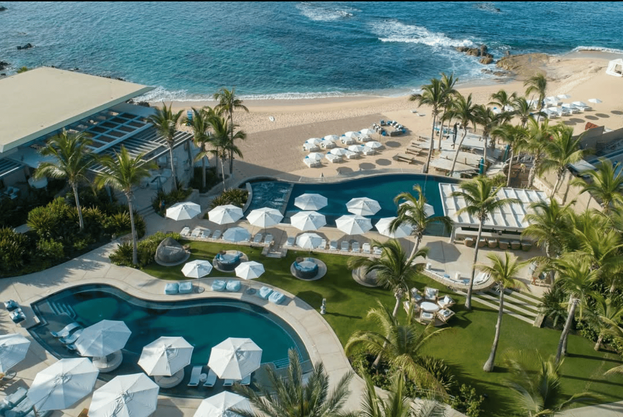 Beachfront resort pools and palm-lined grounds beside the sandy shore and turquoise ocean.