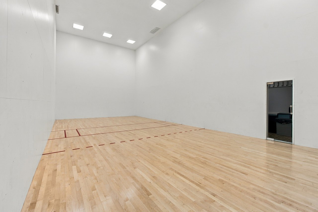 Empty squash court with red floor markings, pale wood flooring, and tall white walls.