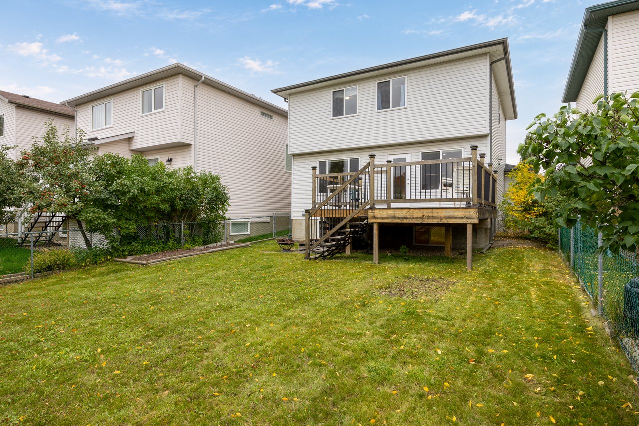 Rear of a two-storey home with a raised deck overlooking a fenced, leafy backyard.