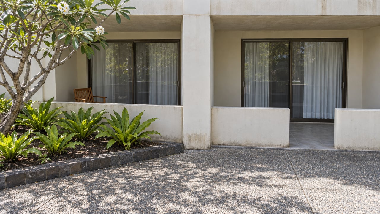 Two recessed lanais in an ivory concrete condominium, beside a flowering plumeria and an exposed-aggregate courtyard.
