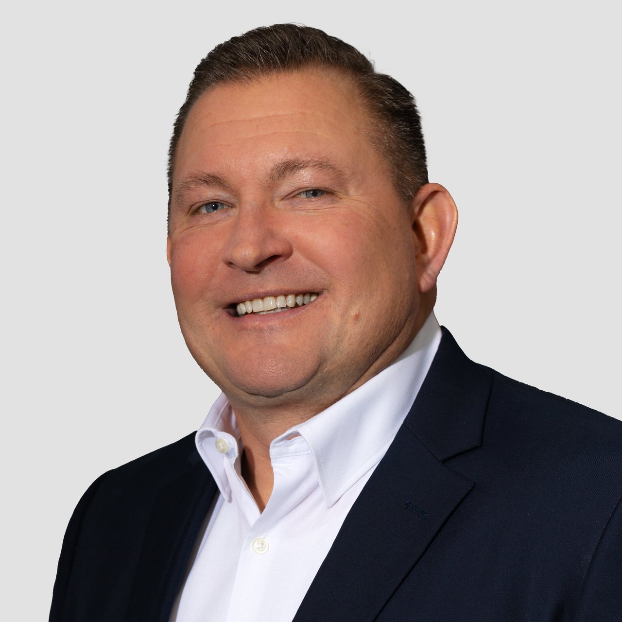 Tim Steinbrecher smiling in a dark suit jacket and white shirt.