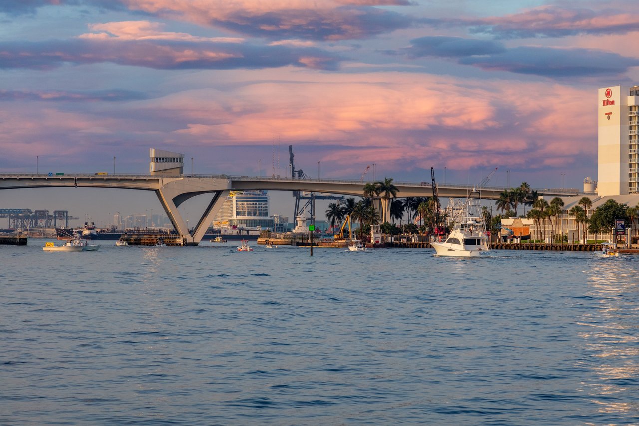 a group of boats in the water with a bridge in the background. The boats are of various sizes and colors. 