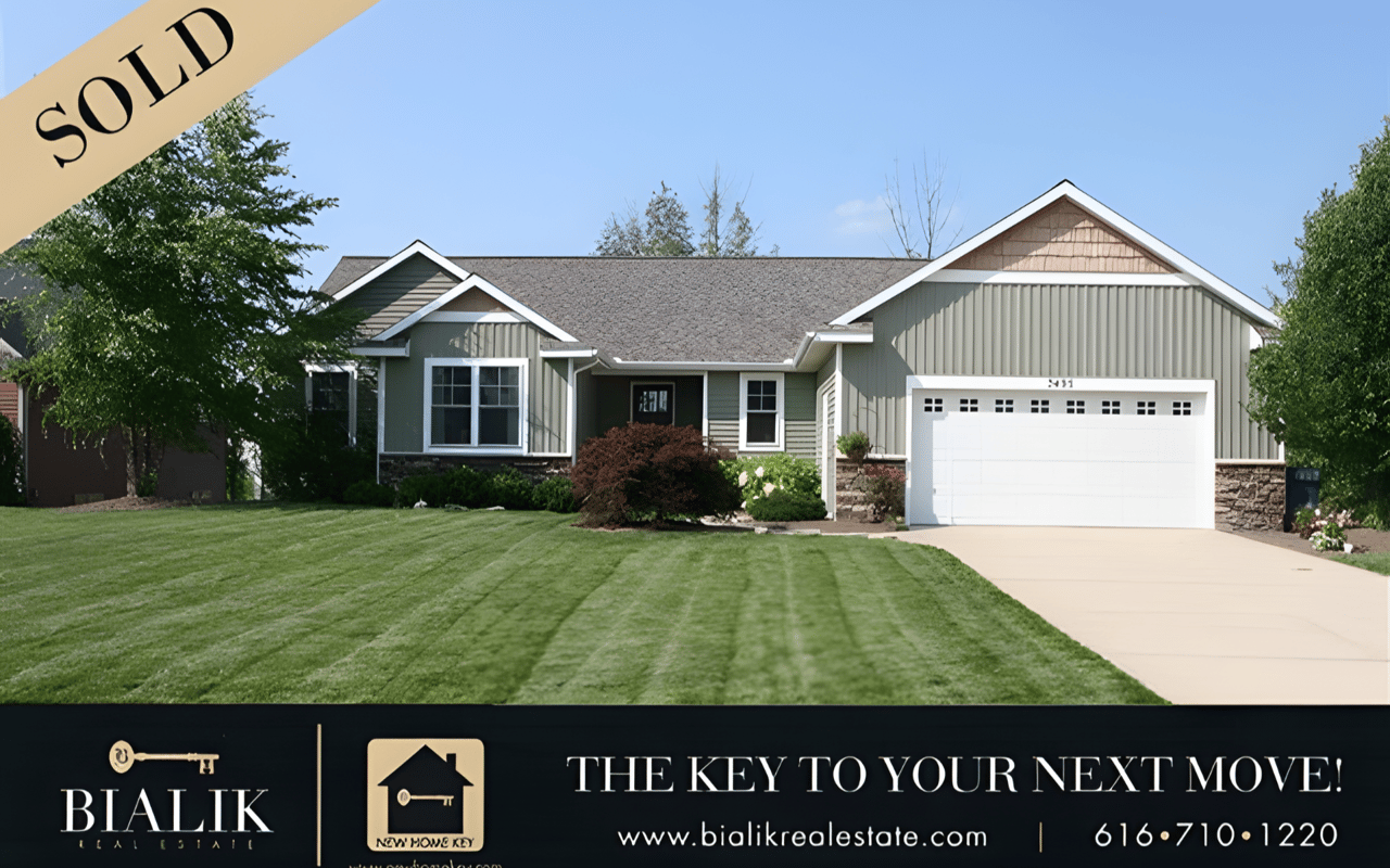 Sold green-gray home with white trim, stone accents, a two-car garage, and a neatly striped lawn.
