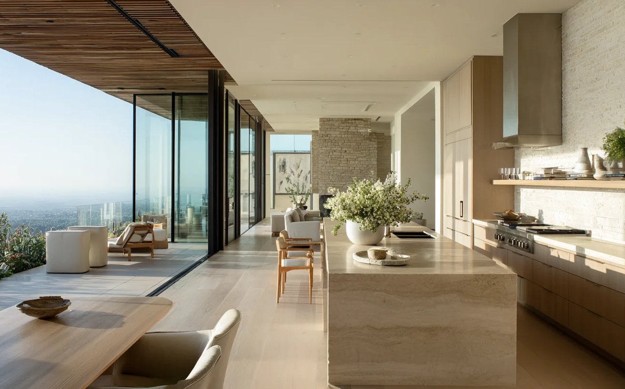 Modern kitchen with a stone island and floor-to-ceiling glass doors overlooking a terrace and distant city.