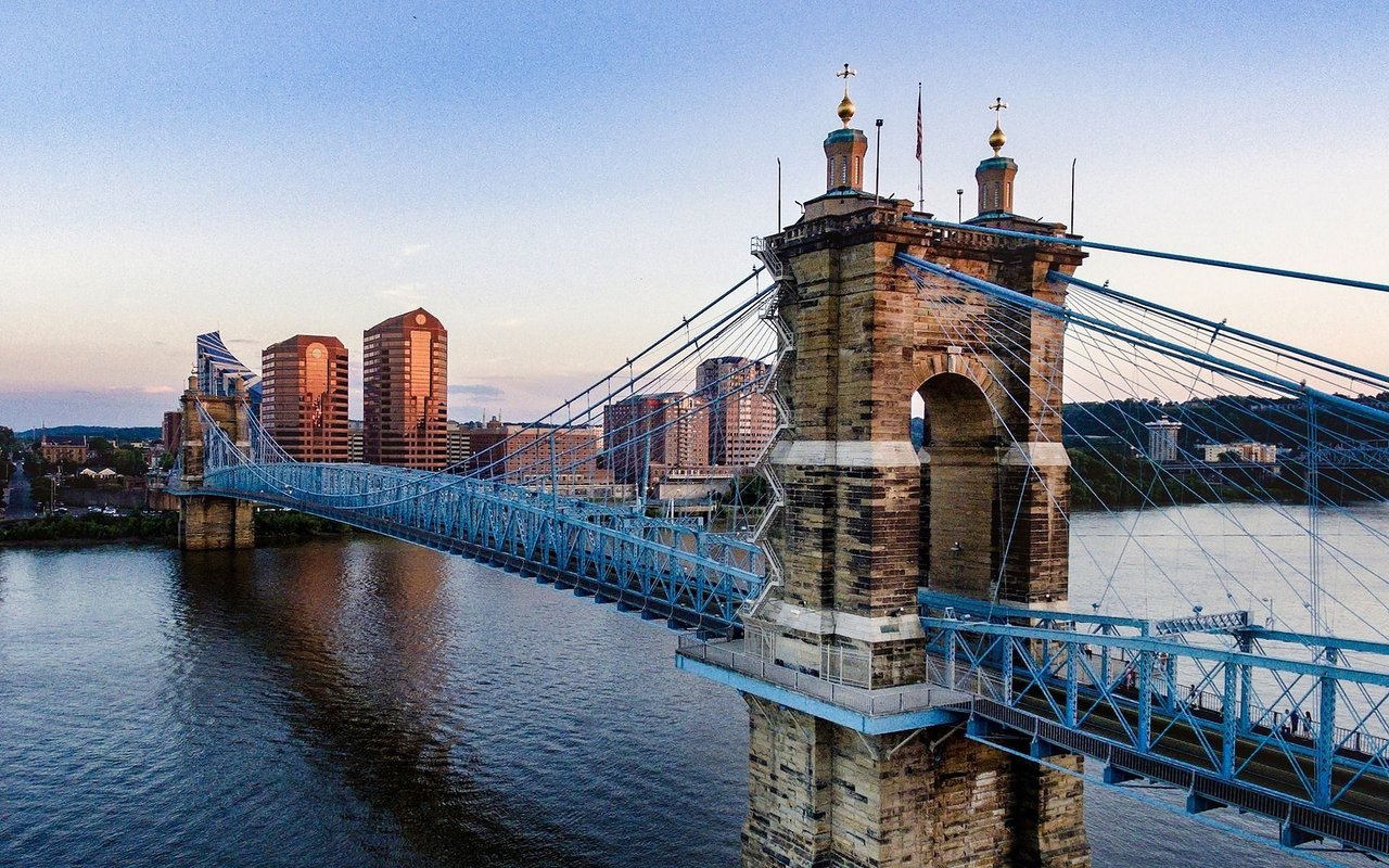 John A. Roebling Suspension Bridge spans the Ohio River with Cincinnati’s skyline at dusk.