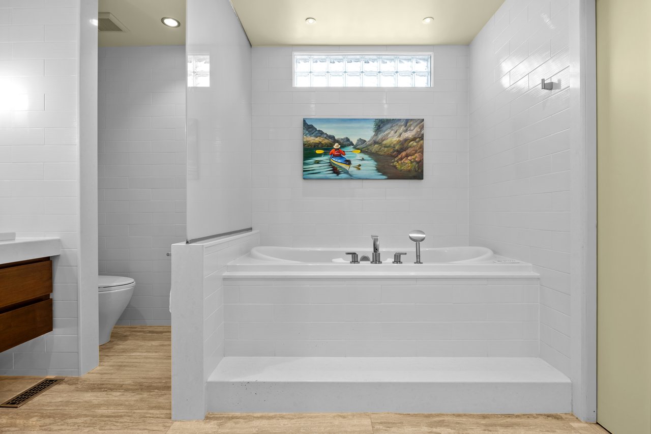 White-tiled bathroom with a large built-in soaking tub beneath a glass-block window.