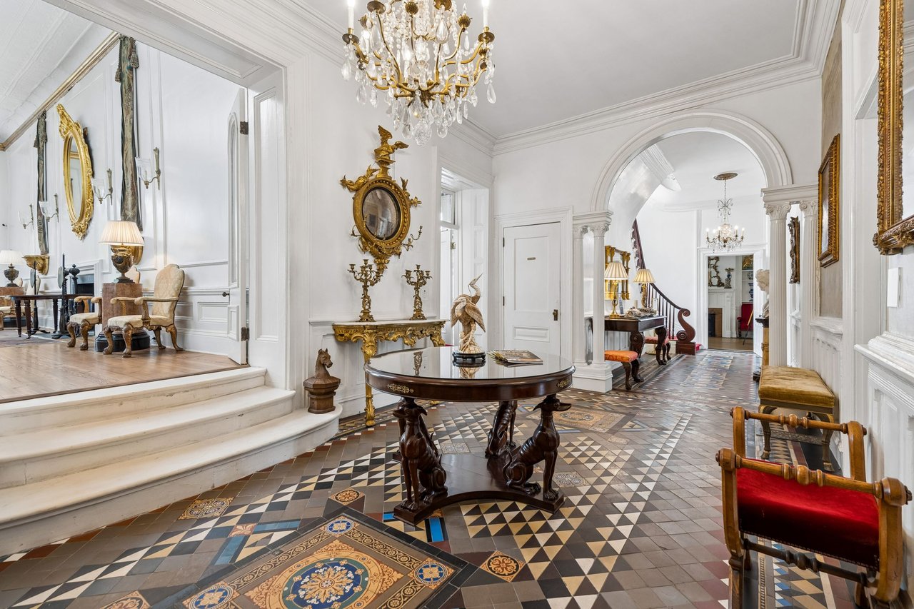 Charleston home's grand foyer with patterned tile floors, a crystal chandelier, and gilded antiques.