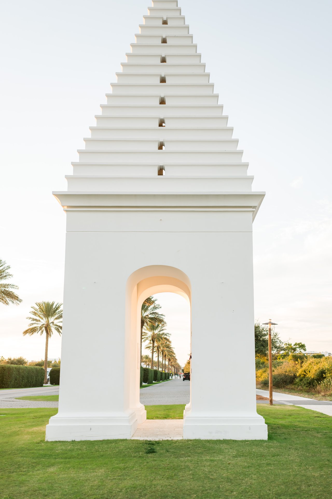 Alys Beach's iconic white stepped-pyramid tower rising from a manicured green lawn against a clear blue sky on 30A, Florida