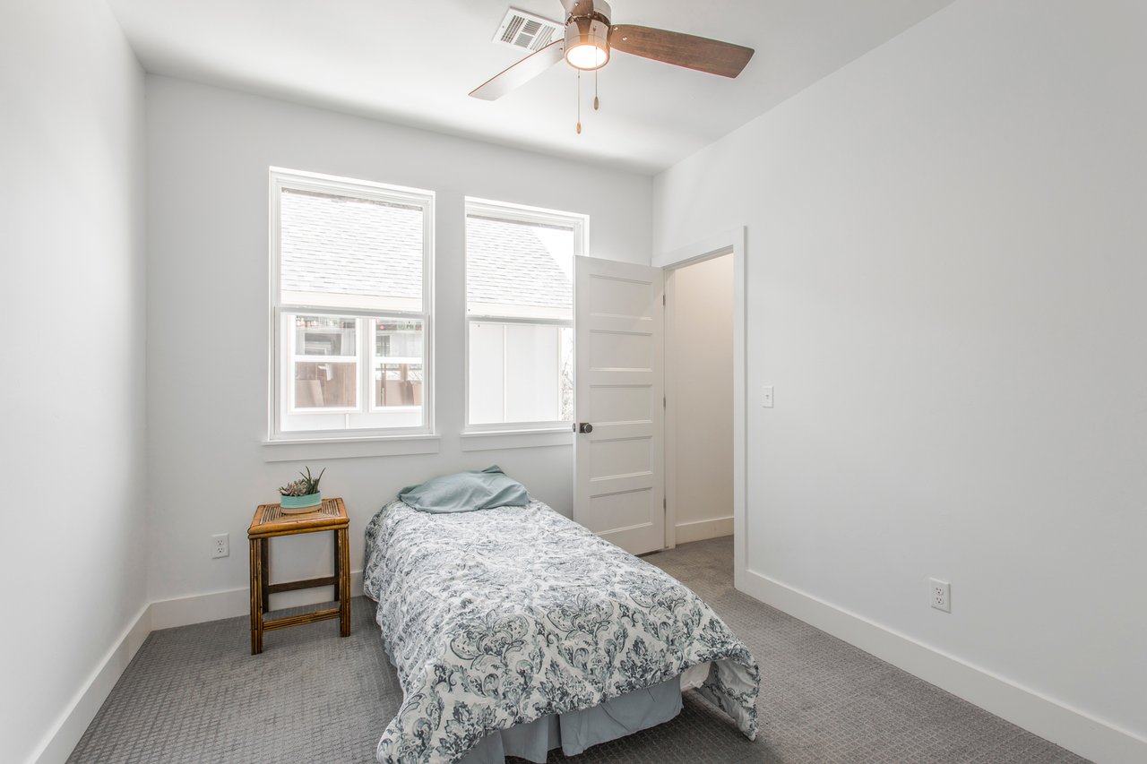 Furnished bedroom with a single patterned bed beneath two windows and a ceiling fan.
