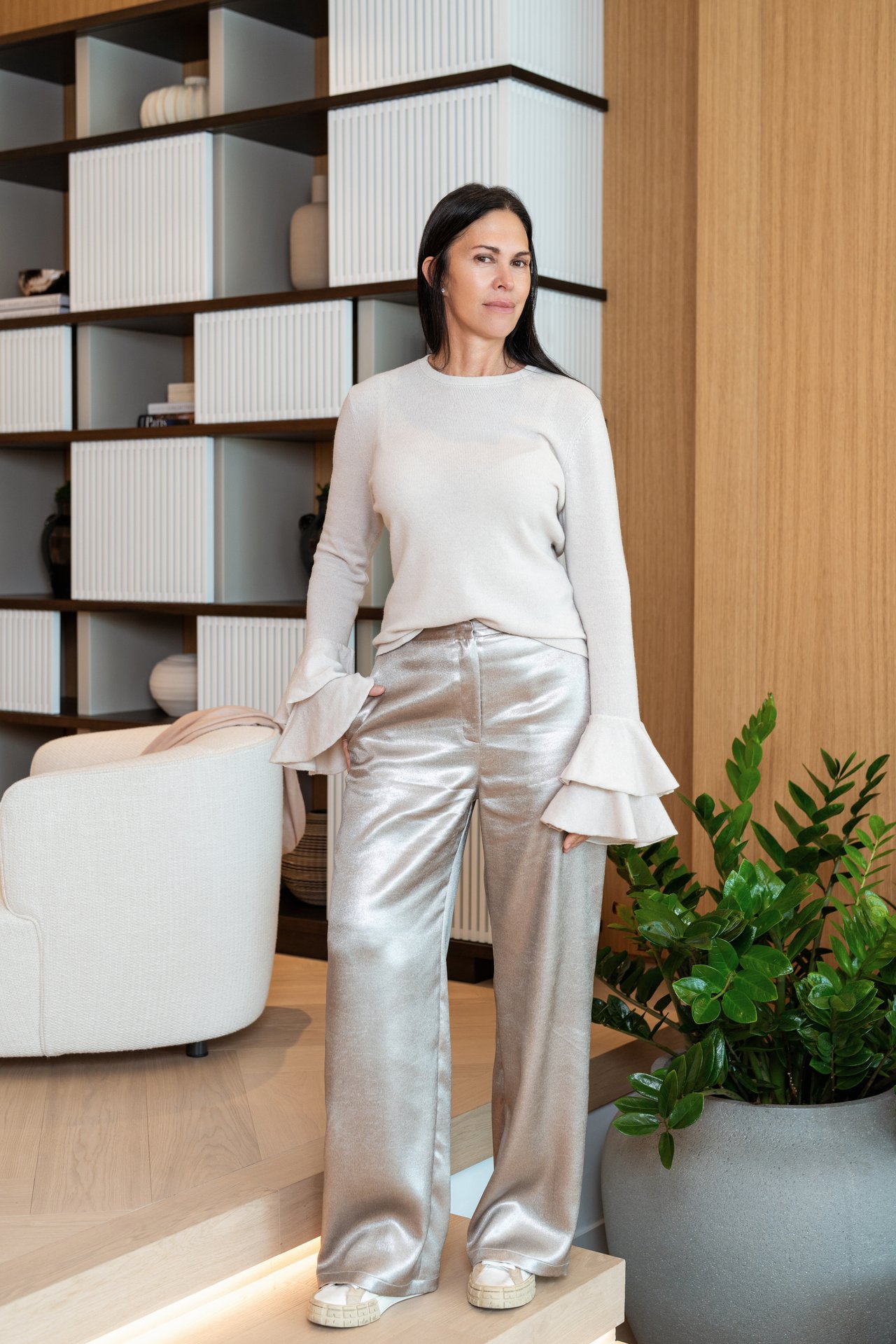 Linda Rinaldi standing beside a white armchair and shelving in a modern interior.