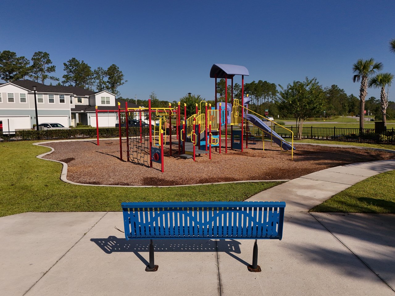 Neighborhood playground with colorful climbing equipment and a blue bench beside the walkway.