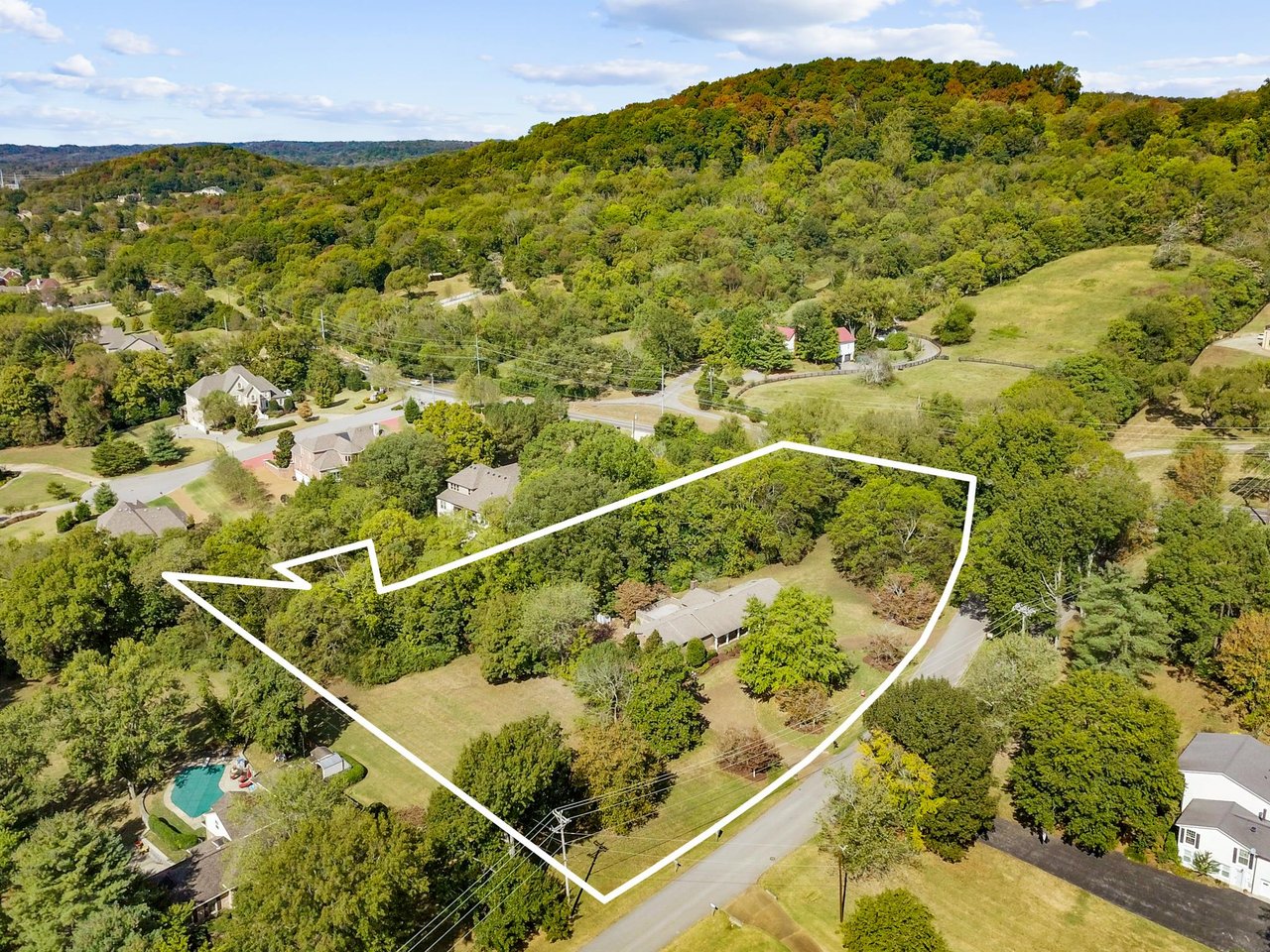 Aerial view of a wooded property outlined in white, with a house and open lawn.
