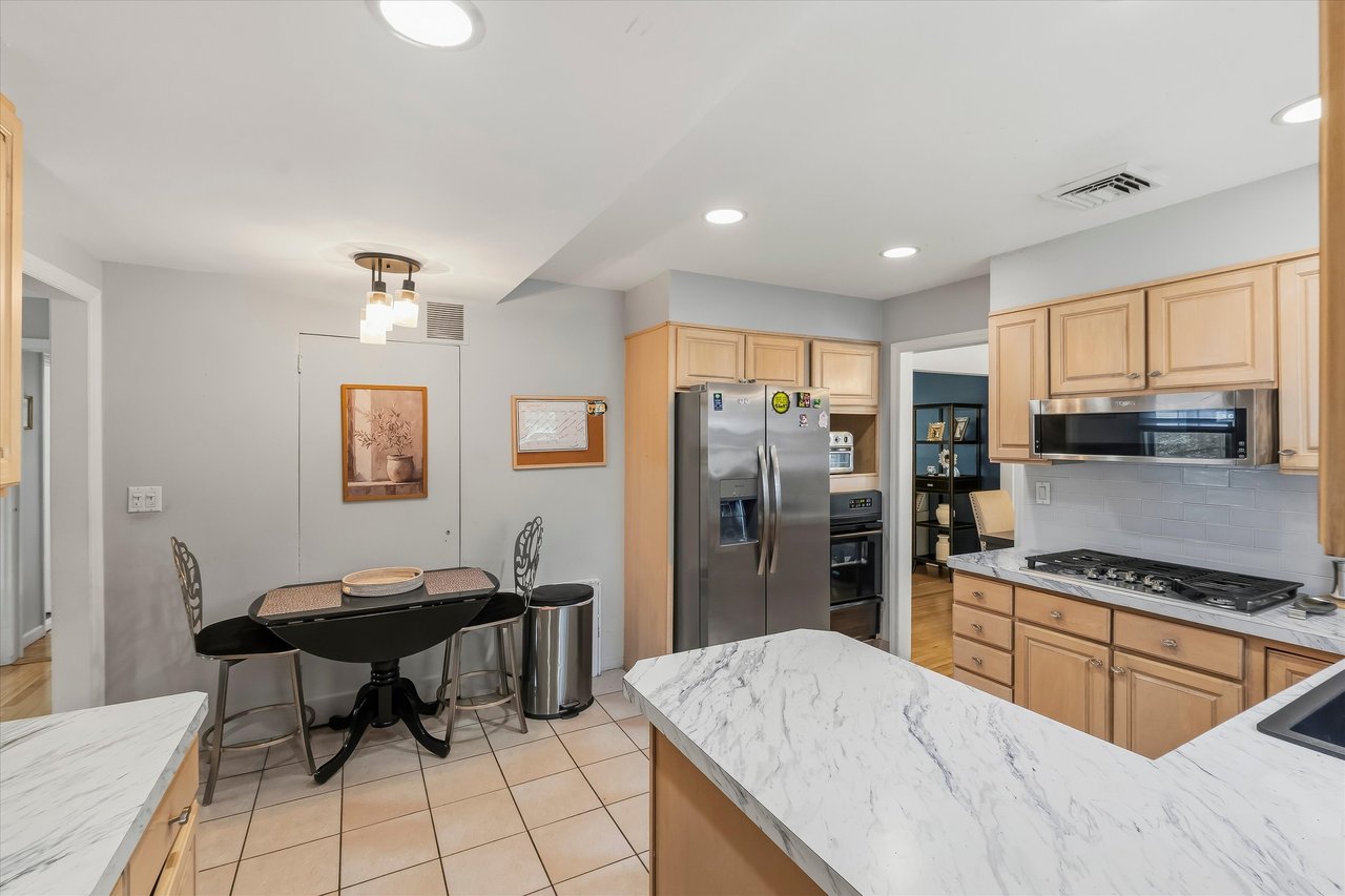 Kitchen with light wood cabinets, stainless steel appliances, and marble-patterned countertops around a large island.