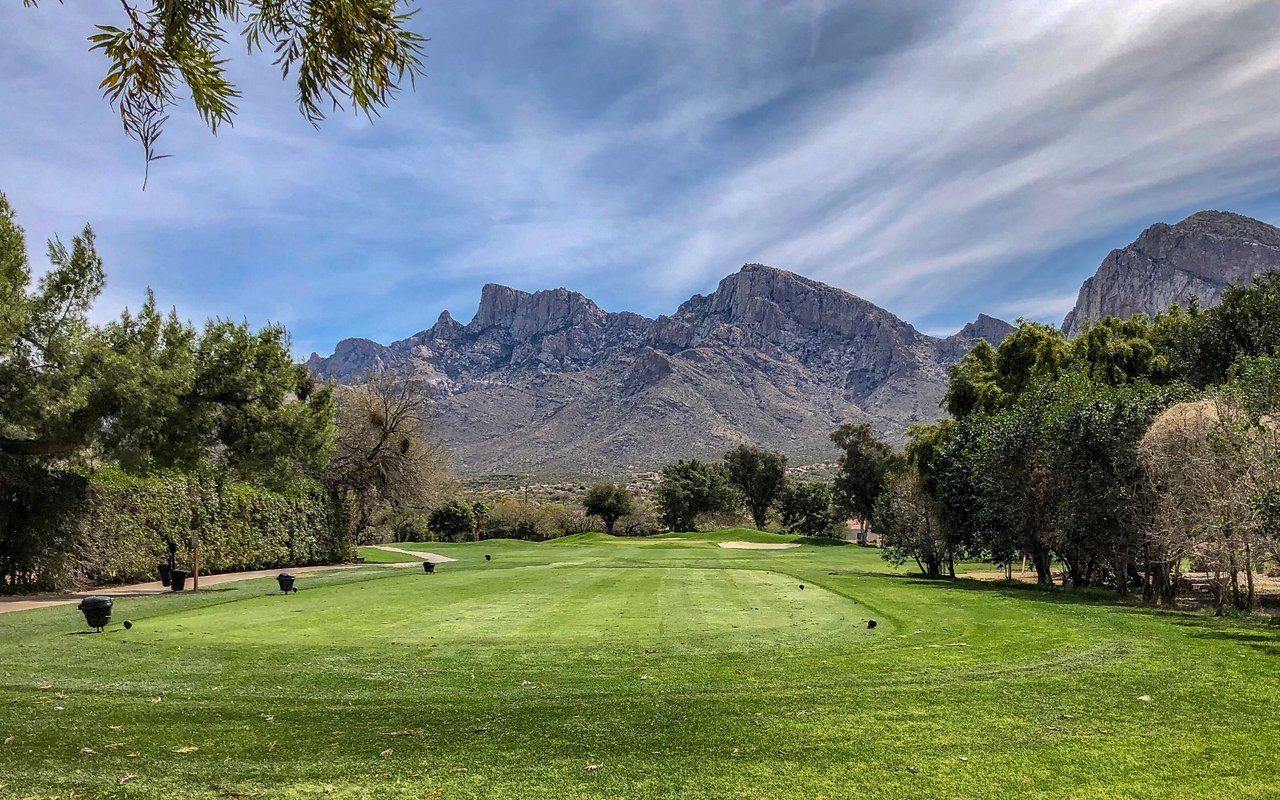 Golf course fairway with rugged mountains rising behind the trees.