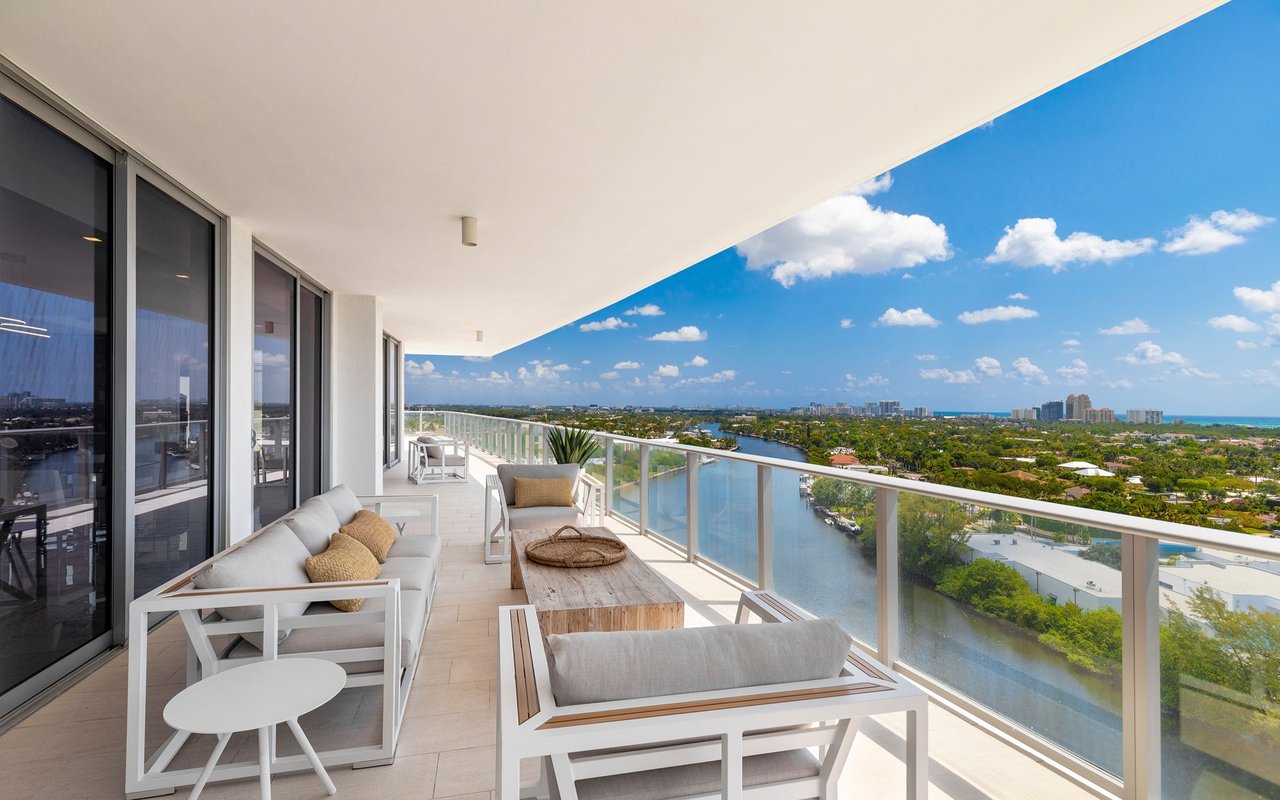 Furnished high-rise condo balcony overlooking a waterway and coastal buildings.