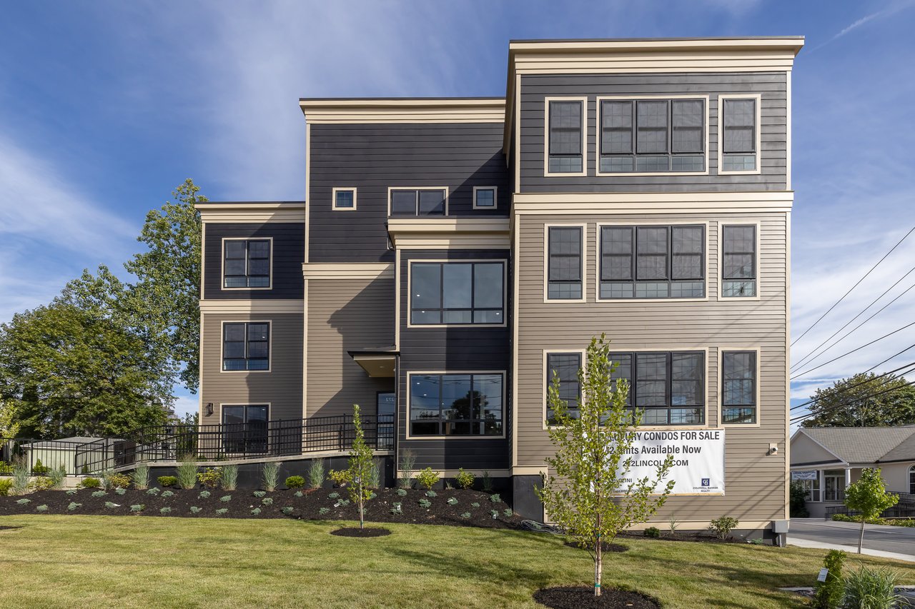 Modern multi-story condominium building with contrasting gray and beige siding and broad windows.