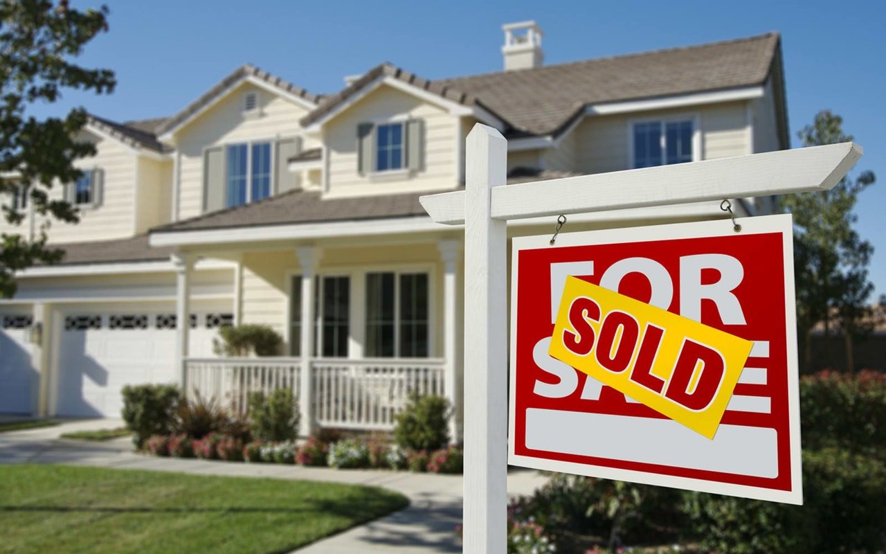 Two-story house with a front porch behind a real estate sign marked SOLD.