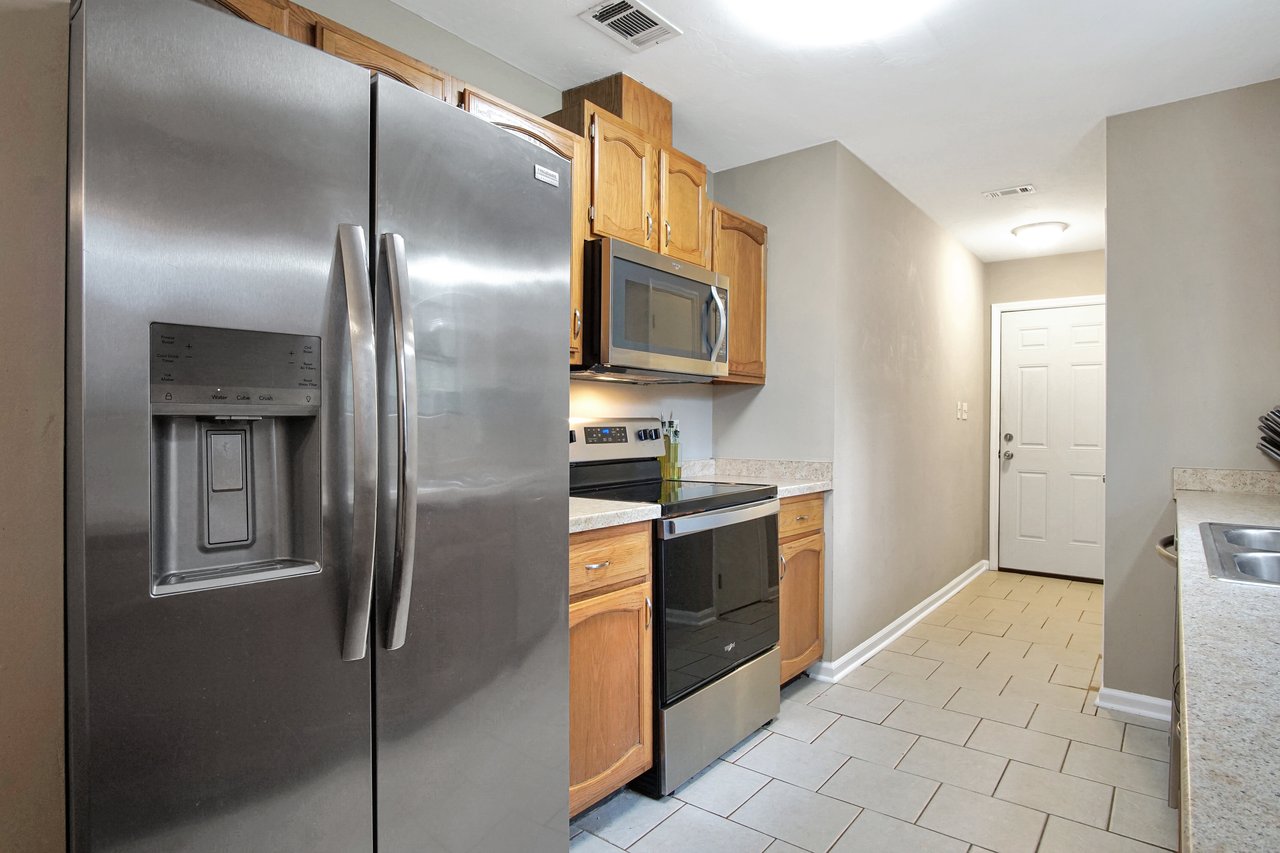 Modern kitchen with stainless steel fridge, oven, and microwave. Wooden cabinets and light tile flooring create a clean and inviting atmosphere.