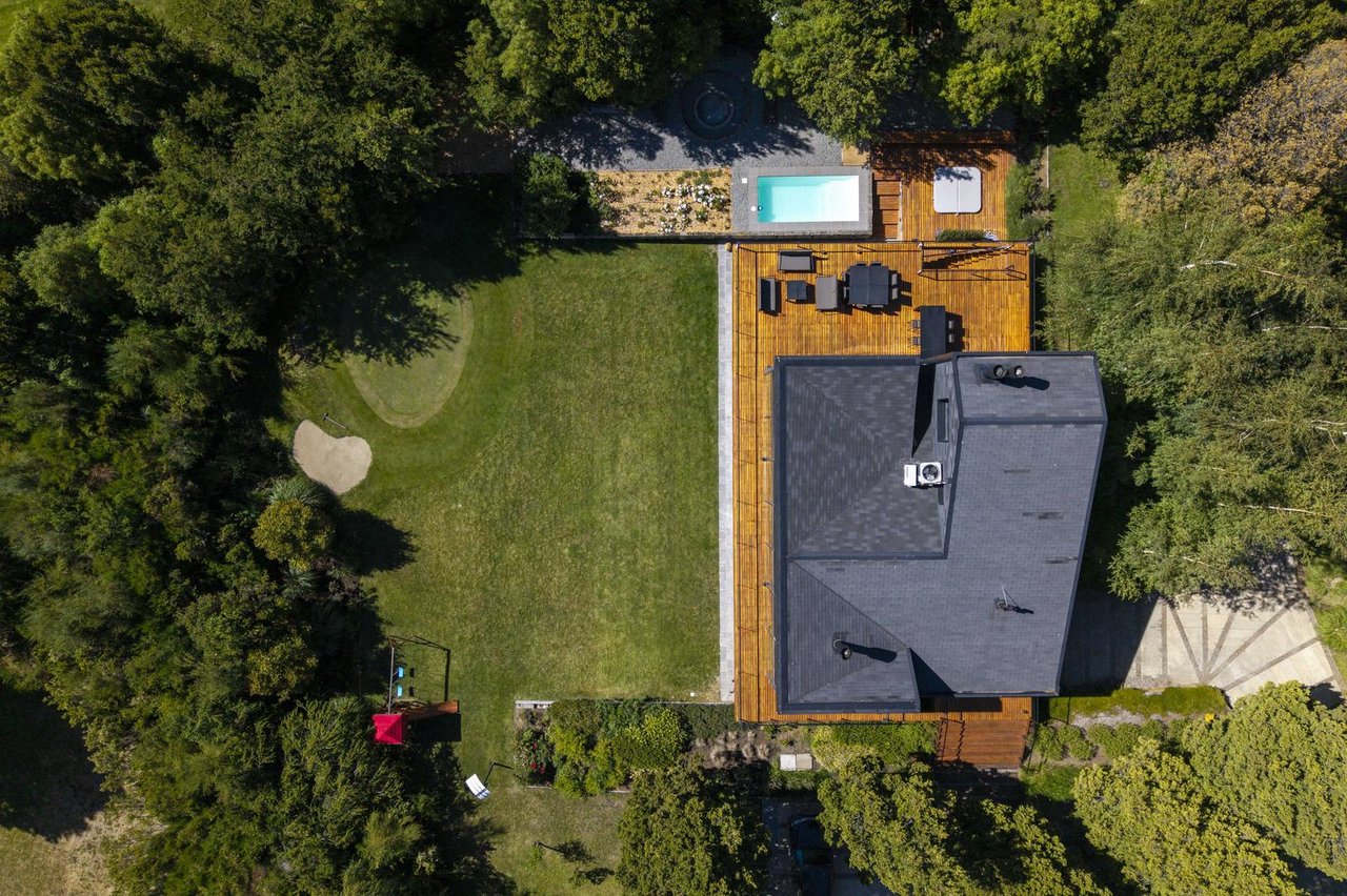 Aerial view of a tree-surrounded house with a wooden deck, outdoor seating, and swimming pool.