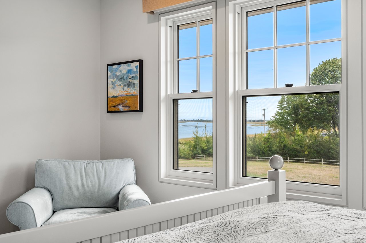 Bedroom with a pale blue armchair and large windows overlooking the water.