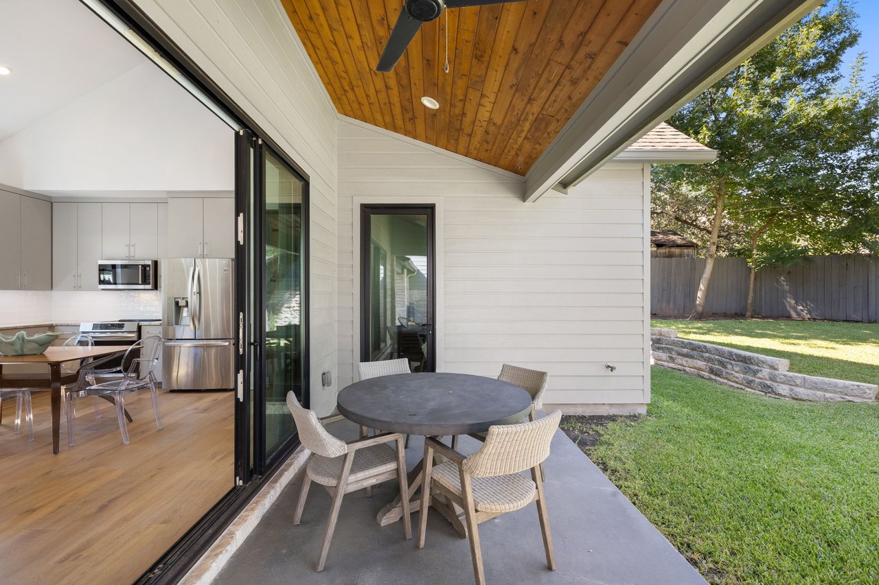 Covered patio with a wood ceiling, round dining table, and open sliding doors to the kitchen.