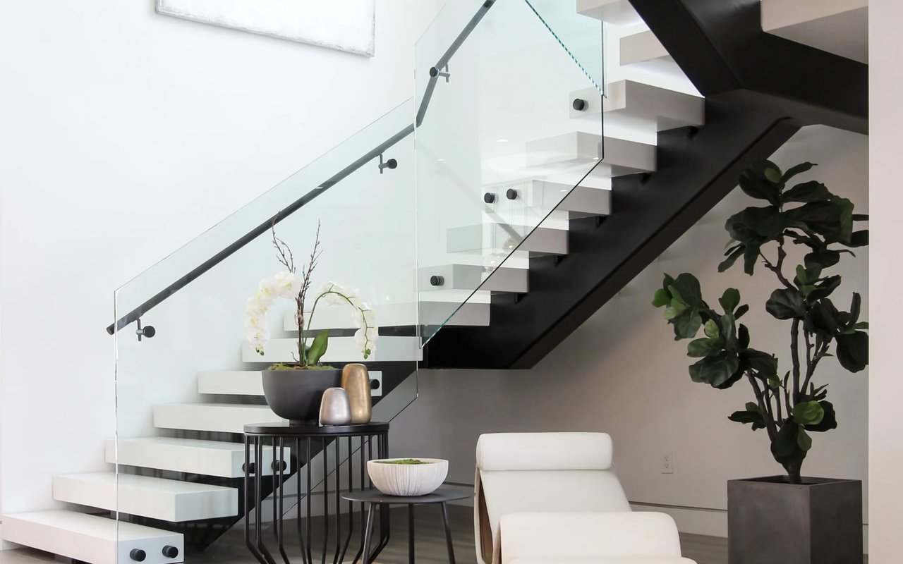 A modern, floating staircase with a glass railing winds up to a second floor.
