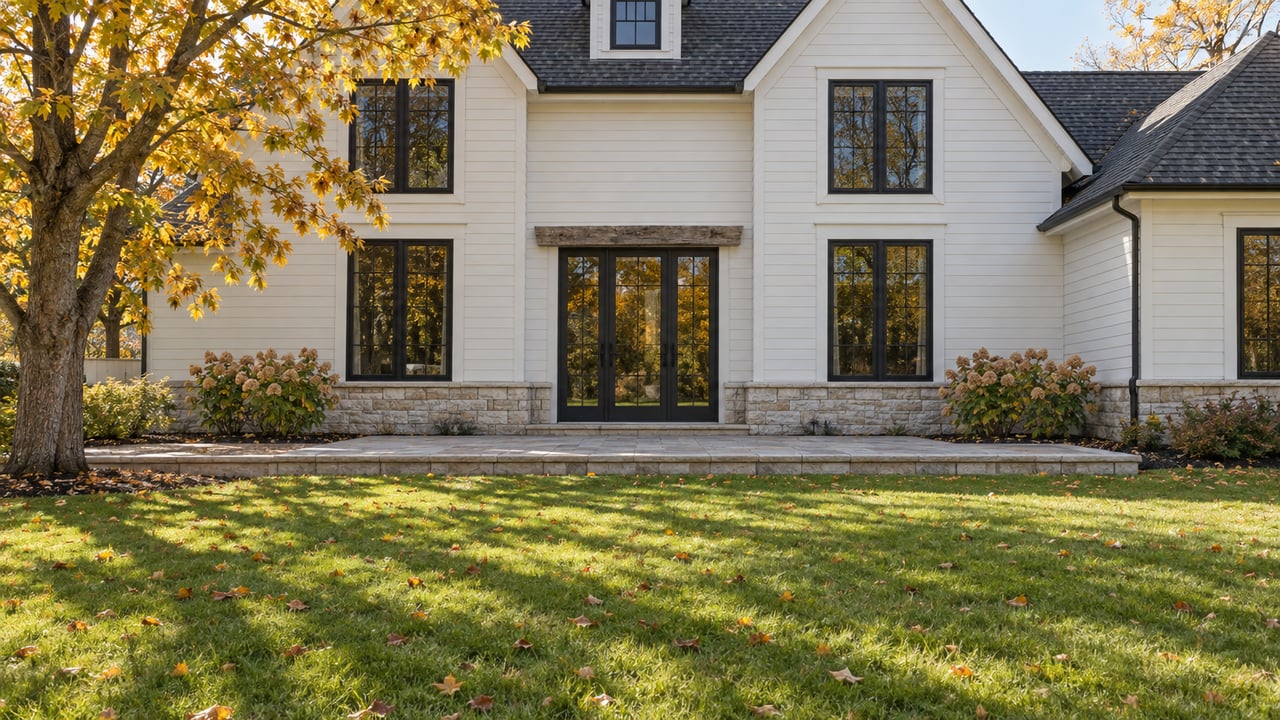 Ivory gabled home with dark-framed windows and a limestone garden terrace beyond an autumn lawn and golden sugar maple.
