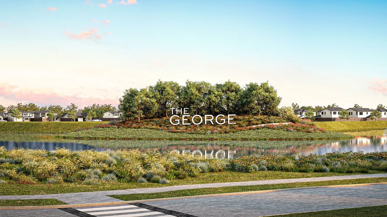 The George community entrance with a landscaped pond, mature trees, and homes along the water.